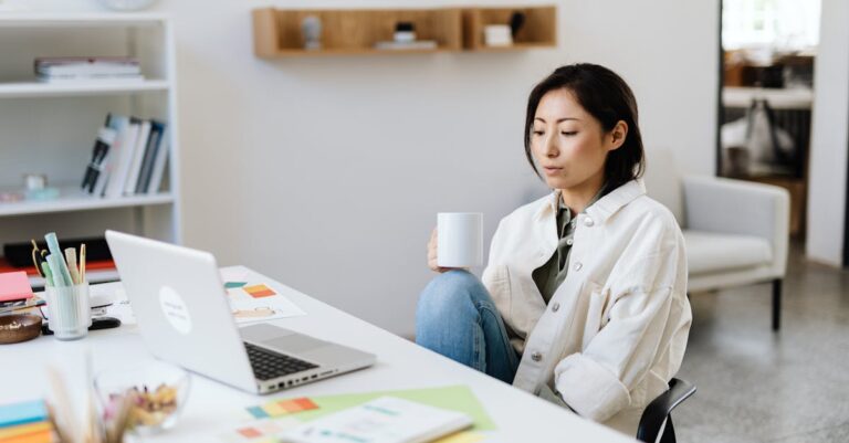 Businesswoman in a modern office setting working on a laptop with a coffee cup.