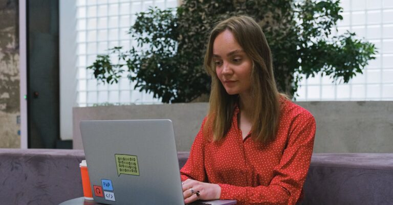 Young woman in red dress using laptop indoors, showcasing remote work lifestyle.