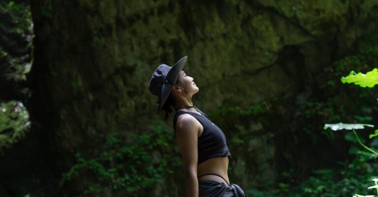 An Asian woman in black clothes admires nature while hiking in a lush green forest.